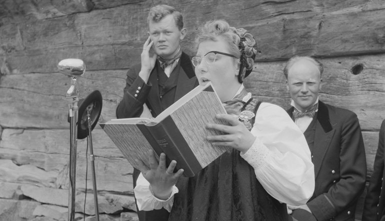 Old photo of someone reading a book into a microphone.