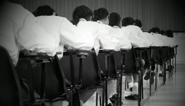 Black and white picture of uniform students sitting at desks.