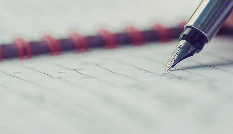 Picture of a pen writing in a notebook.
